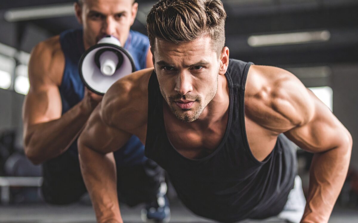 Man doing push-ups, trainer with megaphone.