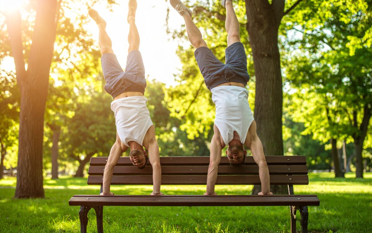 Two men doing handstands on bench.