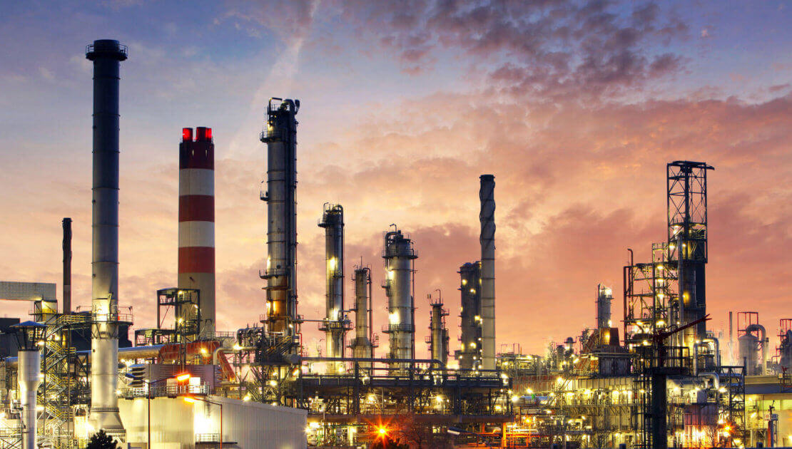 Industrial refinery at sunset with lit towers.