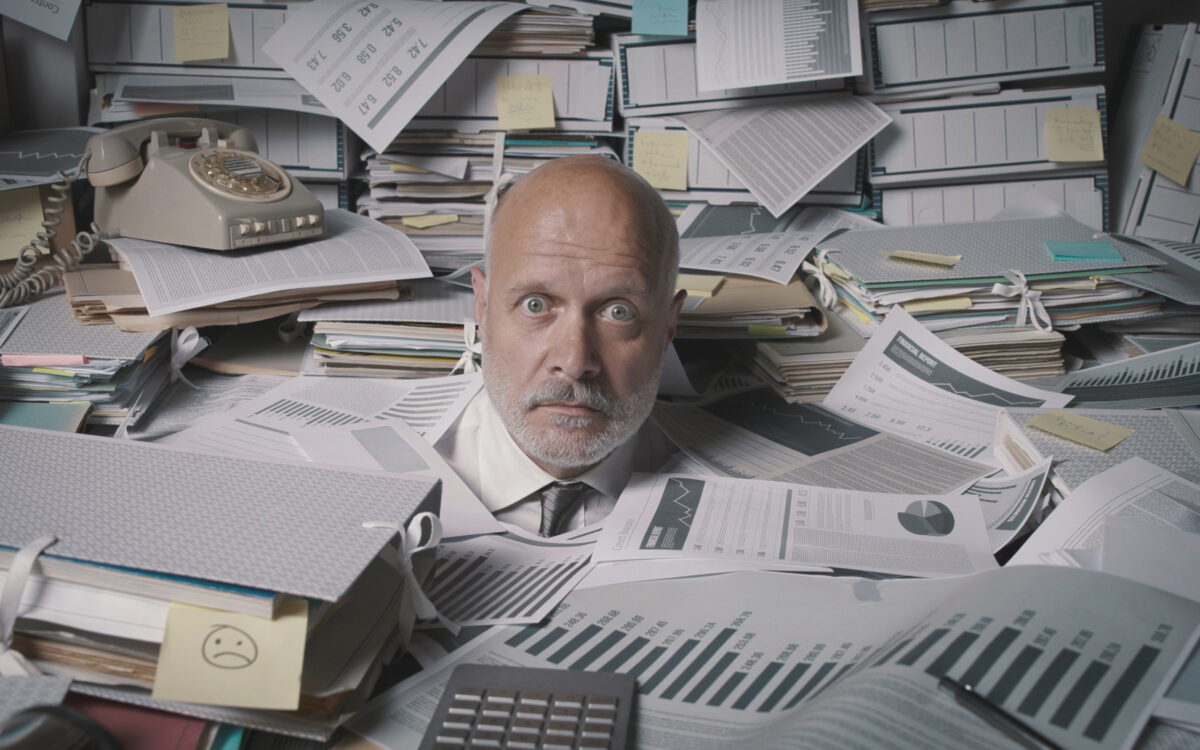 Man overwhelmed by paperwork at desk.