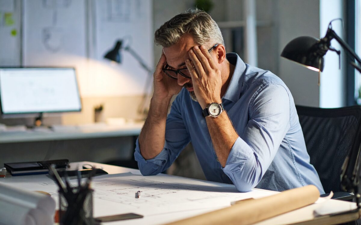 Man stressed at work desk with plans.