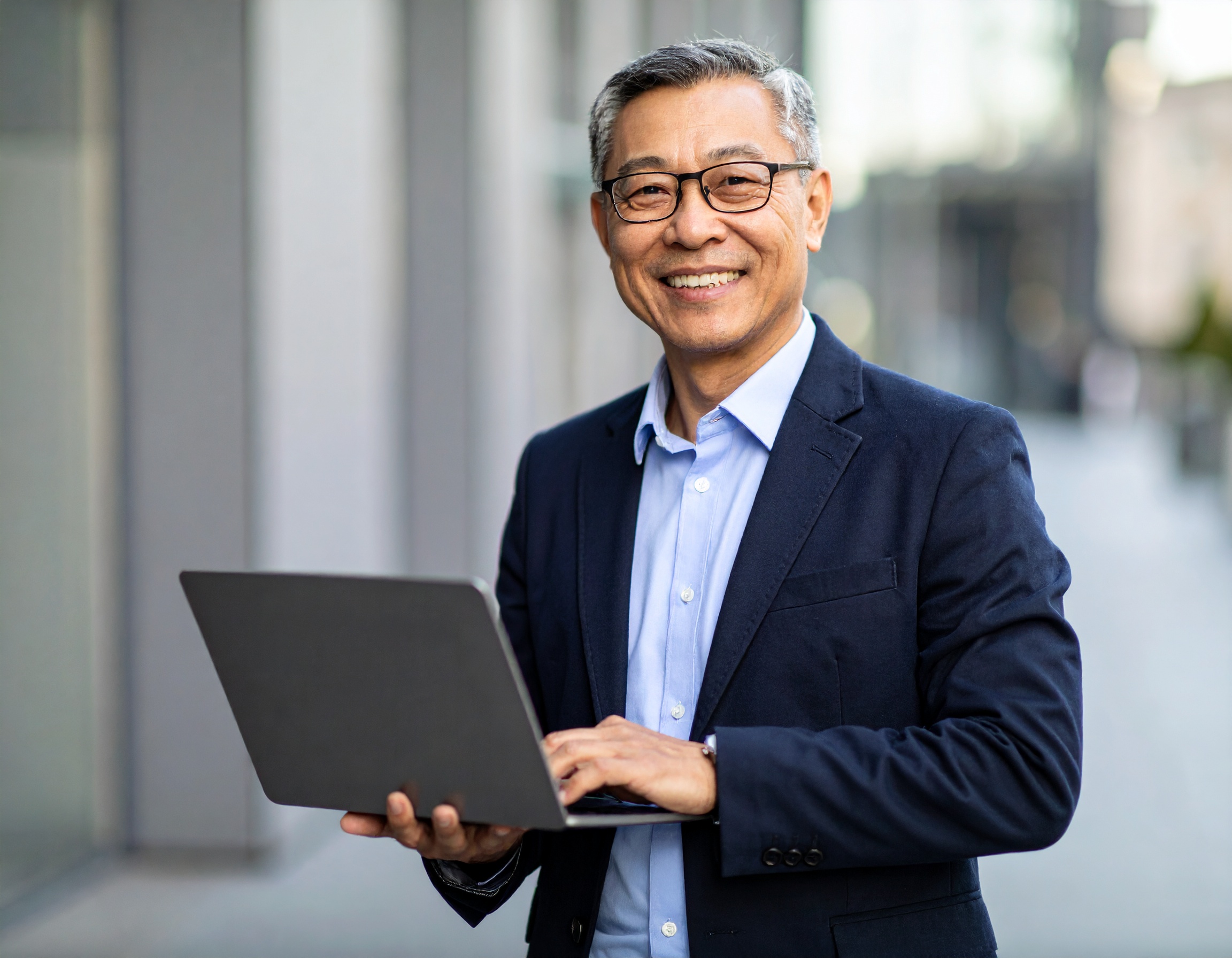 Man smiling while using a laptop outdoors.