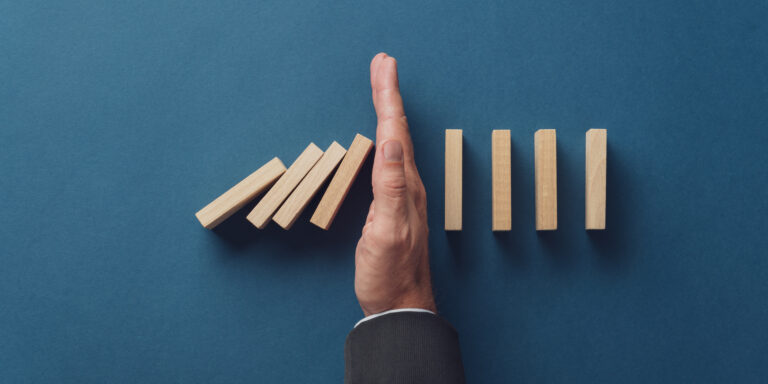 Hand stopping falling wooden dominoes.
